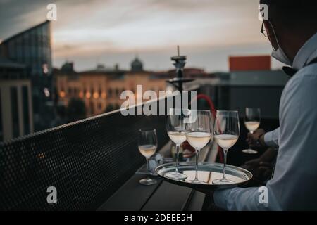 Ein Kellner hält ein Tablett mit Gläsern Weißwein Darauf und serviert sie den Gästen auf dem Balkon Stockfoto