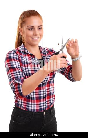 Schöne junge Rothaarige Frau lächelt und schneidet eine Zigarette mit einer Schere, isoliert auf weißem Hintergrund. Fröhliches Mädchen aufgeben Rauchen. Stockfoto