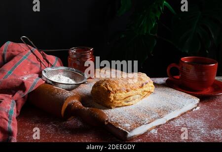 Fresh Puff mit Pflaume oder rote Johannisbeere Marmelade auf dem Tisch mit einer roten Tasse und Glas Marmelade auf dem schwarzen Hintergrund besetzt. Stockfoto