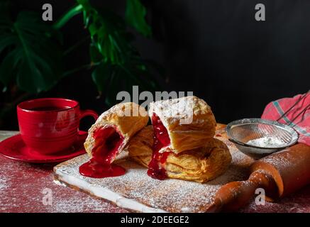 Fresh Puff mit Pflaume oder rote Johannisbeere Marmelade auf dem Tisch mit einer roten Tasse und Glas Marmelade auf dem schwarzen Hintergrund besetzt. Stockfoto