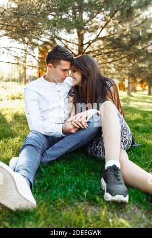 Junges, glückliches, liebevolles Paar, zusammen auf dem Gras im Park sitzend, und sich gegenseitig genießend, Werbung, Stockfoto