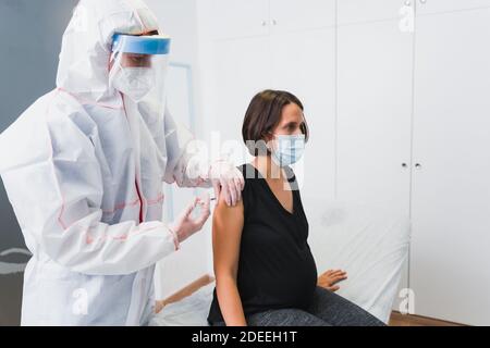 Arzt, der einer schwangeren Frau einen Impfstoff gegen Covid 19 oder Grippe oder Keuchhusten verabreicht. Stockfoto