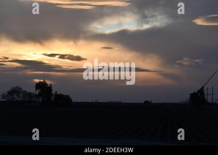 Eine dramatische Wolkenlandschaft bei Sonnenuntergang über einem kultivierten Feld Stockfoto