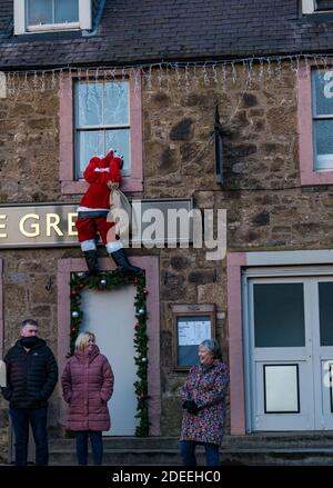 Haddington, East Lothian, Schottland, Großbritannien, 30. November 2020. Weihnachtsdekoration: Das Pub-Restaurant Green hat eine amüsante festliche Darstellung mit einer Santa-Figur, die die Wand in ein Fenster hinaufklettert Stockfoto