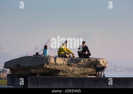 Zwei Männer plaudern während sie sich im Myrtle Edwards Park in Seattle entspannen, während die Sonne am Mount Rainier in der Ferne am Sonntag, dem 29. November 2020 untergeht. Stockfoto