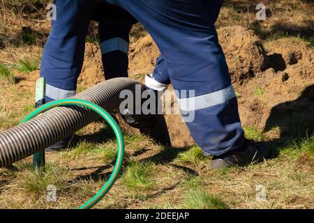 Mann Arbeiter, der Rohr hält und die Reinigung der Kanalisation im Freien bereitstellt. Die Abwasserpumpmaschine verstopft verstopfte Mannlöcher Stockfoto