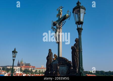 Kruzifix und Statuen von religiösen Figuren und Heiligen auf der Karlsbrücke über die Moldau mit Burg dahinter, Prag, Tschechien Stockfoto