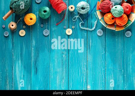 Wollbündel, Garnkugeln, Knöpfe und Kordel. Riegel und Stricknadeln auf bekleidtem türkisfarbenem Holz Stockfoto