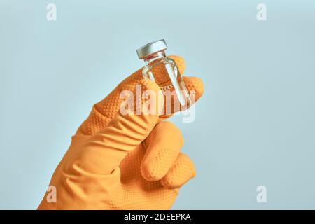 Wissenschaftler hält Impffläschchen, Nahaufnahme der Hand in schützenden Gummihandschuh mit Medizin in Glasflasche Stockfoto