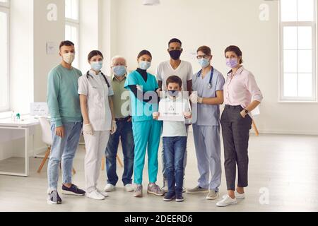 Gruppe von Erwachsenen mit kleinen Jungen, alle in Gesichtsmasken, ruft die Menschen für die Impfung Stockfoto