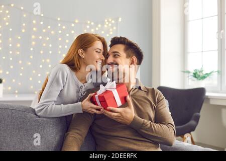 Glücklicher junger Mann hält Valentine Geschenk, lächelnd und dankt seiner Freundin für Geschenk Stockfoto