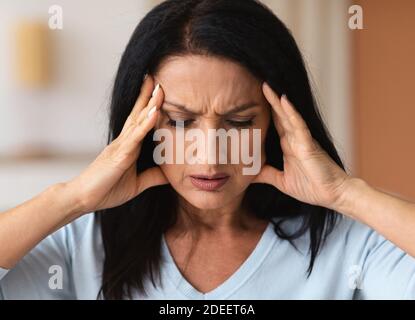 Reife Brünette Frau berühren ihre Tempel Gefühl Stress Stockfoto
