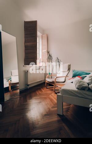 Gemütliche Ecke im Schlafzimmer. Fenster mit hölzernen Fensterläden. Blumentopf. Moderner Stuhl vor dem Fenster Stockfoto