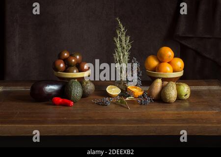 Eine Gruppe von Früchten, Gemüse und aromatischen Kräutern in handgefertigten Tonschüsseln auf einer eleganten Kastanienholzplatte und einem alten strukturierten Hintergrund. Stockfoto