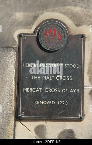 Ayr, Ayrshire, Schottland, Großbritannien. Plage an der Wand, die auf den ehemaligen Standort des Malt Cross & Mercat Cross von Ayr hinweist, wurde 1778 entfernt. Das Malzkreuz wurde 1662 an der Stelle eines früheren Kreuzes errichtet. Es wurde nach dem Vorbild des Marktkreuzes von Edinburgh.in der Straße gegenüber ist ein Steinkreuz in Kopfsteinpflaster in der Straße angelegt Stockfoto