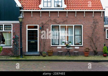 Fassade des holländischen Hauses mit Neujahrsdekorationen. Volendam Dorf in Weihnachten. Gartenmöbel in der Nähe eines Backsteinhauses in den Niederlanden. Feenaltes Haus. Stockfoto