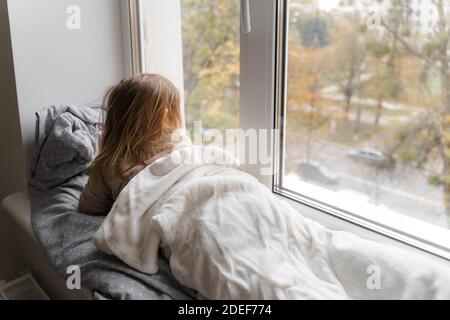 Kind liegt am Fenster im Wohnzimmer und beobachten auf der Straße. Gemütliches Zuhause an Wochenenden, Feiertagen und Absperrung Stockfoto