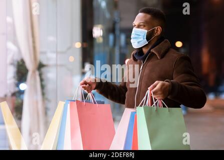 Schwarzer Mann in Maske mit Einkaufstaschen und Blick auf die Mall Stockfoto