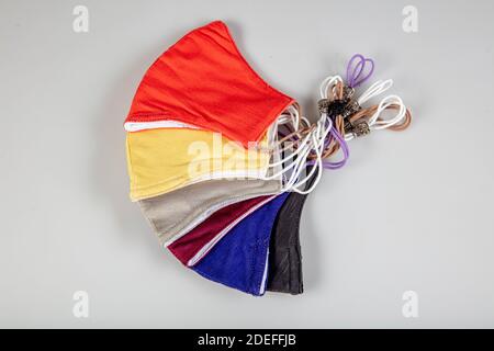Drei gefaltete Gesichtsmasken mit elastischen Ohrschlaufen - gestapelt, weiße Maske oben, blau und schwarz im Hintergrund. Wiederverwendbare waschbare Masken aus Baumwollgewebe in h Stockfoto