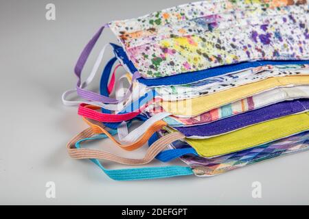 Drei gefaltete Gesichtsmasken mit elastischen Ohrschlaufen - gestapelt, weiße Maske oben, blau und schwarz im Hintergrund. Wiederverwendbare waschbare Masken aus Baumwollgewebe in h Stockfoto