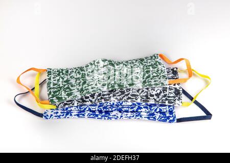 Drei gefaltete Gesichtsmasken mit elastischen Ohrschlaufen - gestapelt, weiße Maske oben, blau und schwarz im Hintergrund. Wiederverwendbare waschbare Masken aus Baumwollgewebe in h Stockfoto