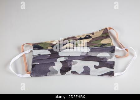 Drei gefaltete Gesichtsmasken mit elastischen Ohrschlaufen - gestapelt, weiße Maske oben, blau und schwarz im Hintergrund. Wiederverwendbare waschbare Masken aus Baumwollgewebe in h Stockfoto