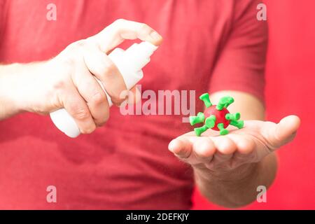 Männliche Hand sprüht antiseptisch auf eine Zelle des COVID-19 Influenza-Virus auf einem roten Hintergrund. Stockfoto