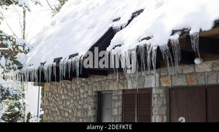 Das Dach des Hauses ist mit Schnee und großen Gletschern bedeckt, die sich an der Rinne gebildet haben.Eis hängt.Winterwetter. Stockfoto