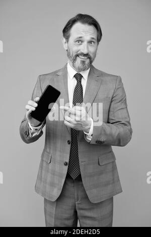 Selbstbewusster Mann in smart Casual Wear halten Smartphone. Zeigefinger auf digitales Gerät. Social Network. Experte im digitalen Marketing. Reife General Manager. Männliche Business Executive. Stockfoto