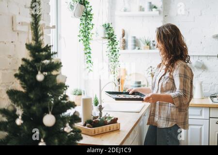 Attraktive lächelnde Frau mit lockigen Haaren in karierten Hemdbäcken Kekse in der hellen Küche zu Hause Stockfoto