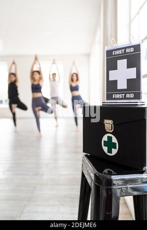 Erste-Hilfe-Box mit seiner Beschilderung für die Sicherheit im Fitness-Studio mit Hintergrund der Yoga-Klasse Studenten und Trainer. Gesunder Lebensstil und Sicherheit erster Sport Stockfoto