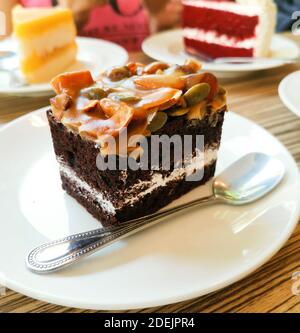 Schokoladen-Toffee-Kuchen und Silberlöffel auf weißem Porzellangeschirr. Stockfoto