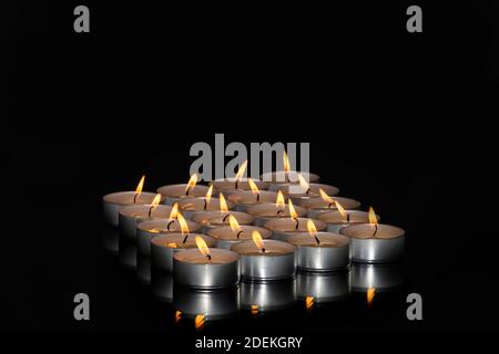 Ansicht einer Anordnung von beleuchteten Teelichtkerzen auf einer reflektierenden Oberfläche auf einem dunklen Hintergrund. Entspannung und abstraktes Konzept. Stockfoto