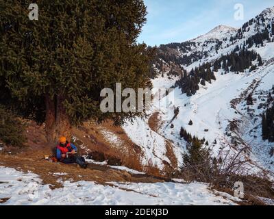 Ein männlicher Tourist trinkt Kaffee bei einem Halt im Winter in den Bergen. Kaffee machen auf einer Wanderung Stockfoto