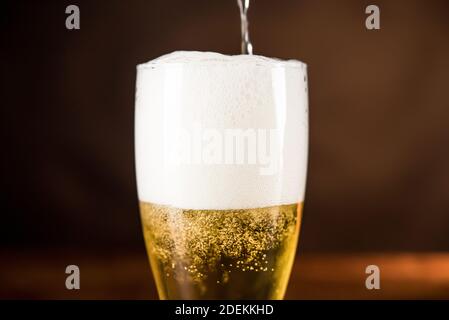 Goldenes kaltes Bier, das mit Schaum ins Glas gegossen wird Schaum Stockfoto