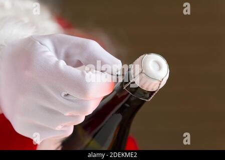 Mann im weihnachtsmann Kostüm öffnet eine Flasche Champagner Stockfoto