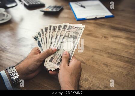 Geschäftsmann, der Geld zählt, japanische Yen-Geldscheine, am Holztisch im Büro Stockfoto