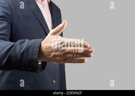 Männlicher Geschäftsmann streut seine Hand für einen Handschlag auf grauem Hintergrund. Geschäftsmann und Gestenthema ein Mann in einem Anzug und Krawatte hält seine Hand Stockfoto