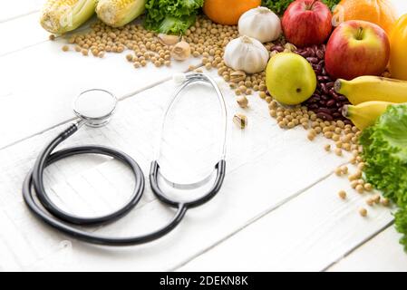 Medizinische und gesunde Lebensmittel, gemischte Früchte und Nüsse, mit Stethoskop auf weißem Holztisch Stockfoto