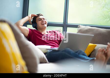 EIN JUNGER COLLEGE-STUDENT LACHEND, WÄHREND VIDEOS AUF LAPTOP Stockfoto