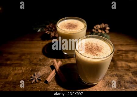 Hausgemachte traditionelle Weihnachten Eierbecher Getränke in den Gläsern mit gemahlener Muskatnuss, Zimt und Dekoration Artikel auf Holztisch, Vorbereitung für die Feier Stockfoto