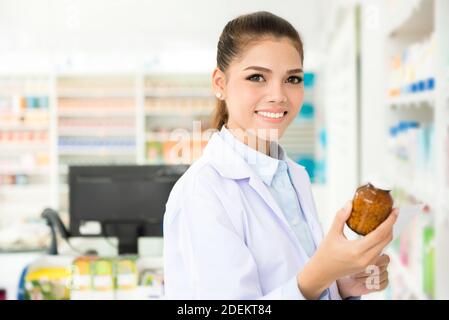 Lächelnde asiatische Apothekerin oder Arzt hält Medizin Flasche und Rezept, Blick auf Kamera, in der Klinik oder Apotheke Stockfoto