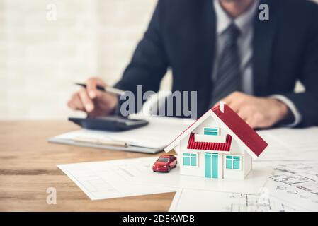 Geschäftsmann Berechnung Budget vor der Unterzeichnung Immobilien-Projekt-Vertrag mit Haus- und Automodell am Tisch im Büro Stockfoto