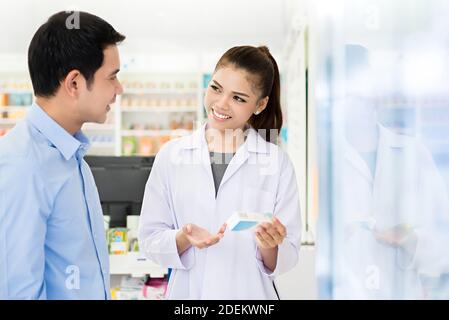 Schöne asiatische Apothekerin oder Arzt erklärt verschreibungspflichtige Medizin zu einem männlichen Kunden in einer Apotheke. Stockfoto