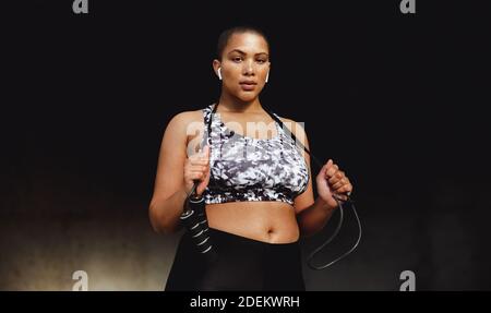 Frau in Fitnesskleidung, die sich während ihres Workouts entspannt und ein Seilspringen hält. Fitness-Frau, die draußen steht und ein Seil hält und ansieht Stockfoto