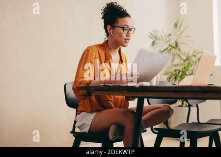 Geschäftsfrau, die Dokumente hält und eine Videokonferenz auf ihrem Laptop anruft. Frau, die von zu Hause aus arbeitet und ein Videogespräch führt. Stockfoto