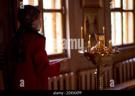 Eine ältere Frau steht vor einer Kerzenleuchter. Auf dem Kerzen angezündet sind. Christliche Kirche Stockfoto