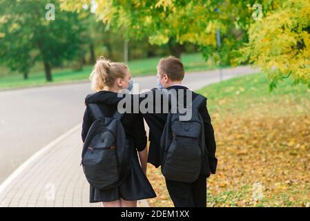 Schüler, Junge und Mädchen in medizinischen Masken gehen im Stadtpark. Stockfoto