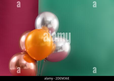 Bündel von metallischen Luftballons schweben auf dunkelrot und grün Hintergrund Stockfoto