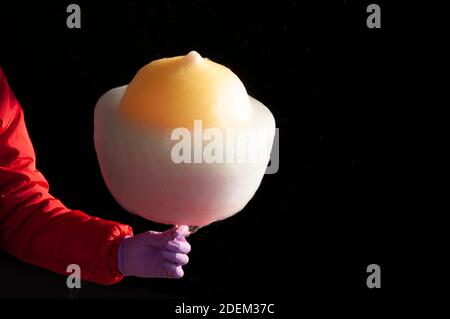 Mann hält süße Zuckerwatte auf Stick vor schwarzem Hintergrund. Hand mit Handschuh. Schutzkonzept. Frohe Kinder. Stockfoto